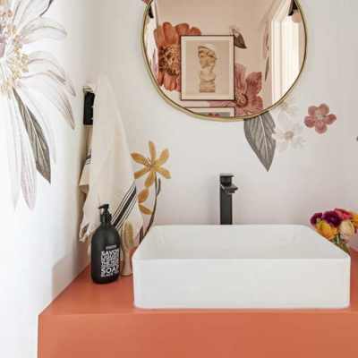 floral wall papered bathroom with orange vanity and gold accents